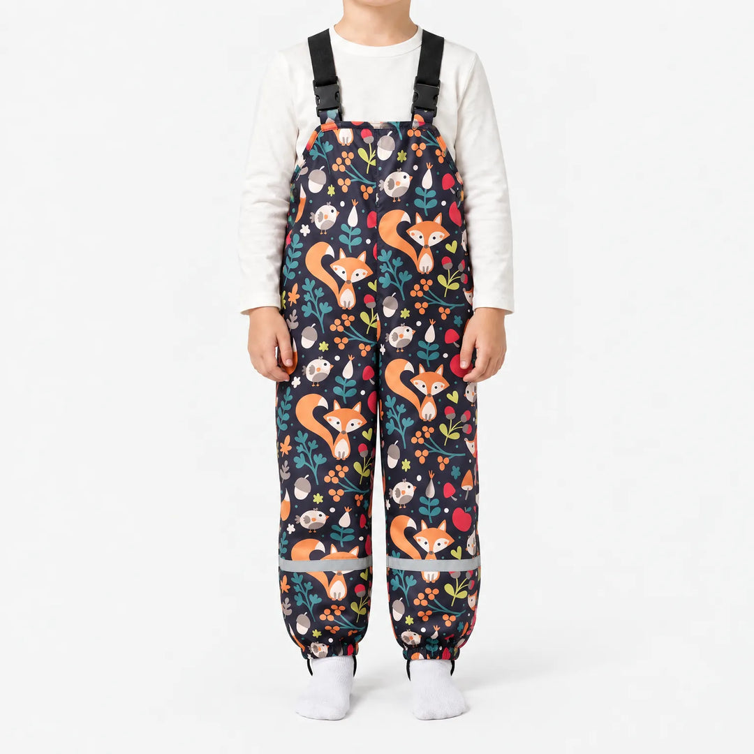 Child in dark navy dungarees printed with orange foxes, birds, acorns, berries and leaves, with buckled straps and reflective ankle bands. 13