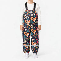 Child in dark navy dungarees printed with orange foxes, birds, acorns, berries and leaves, with buckled straps and reflective ankle bands. 13