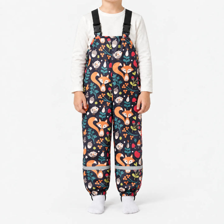 Child in dark navy dungarees printed with orange foxes, birds, acorns, berries and leaves, with buckled straps and reflective ankle bands. 13