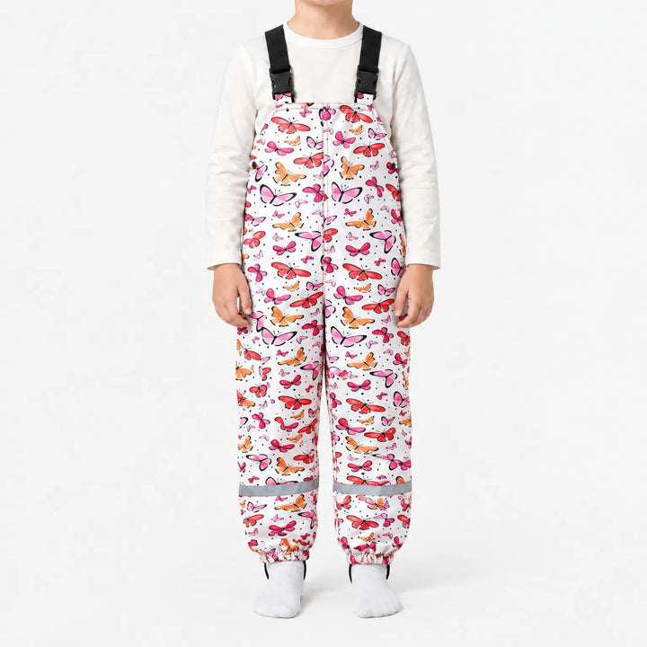 Child in white dungarees covered in pink, red and orange butterflies, with black buckled straps and a reflective strip at each ankle. 14