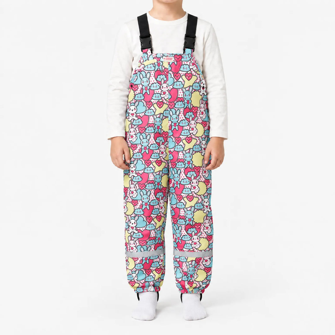 Child in dungarees with a busy pattern of pastel blue and pink bunnies, hearts and clouds, with buckled straps and reflective ankle bands. 15