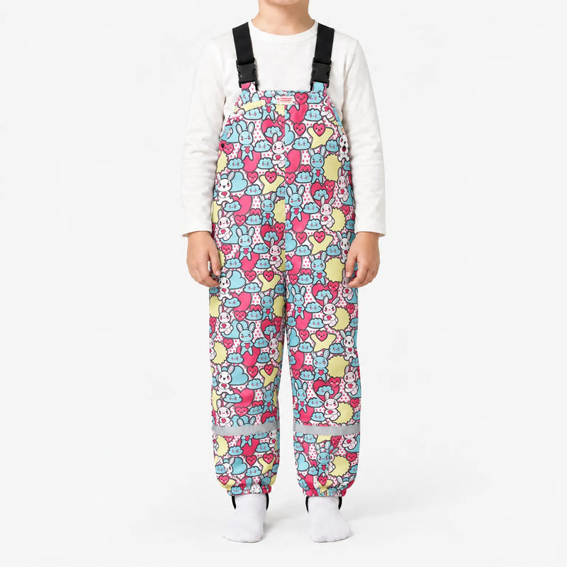 Child in dungarees with a busy pattern of pastel blue and pink bunnies, hearts and clouds, with buckled straps and reflective ankle bands. 15