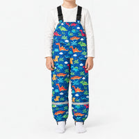 Child in blue dungarees printed with colourful dinosaurs, palm leaves and clouds, with buckled straps and a reflective band at each ankle. 16