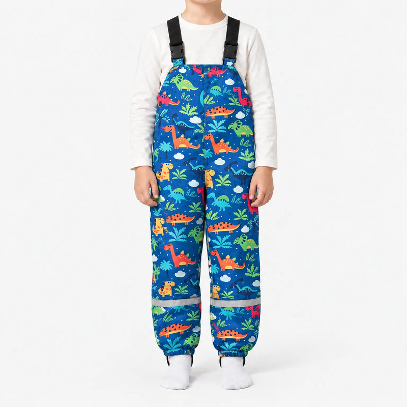 Child in blue dungarees printed with colourful dinosaurs, palm leaves and clouds, with buckled straps and a reflective band at each ankle. 16