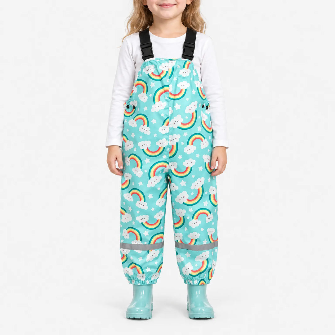 Smiling girl wearing turquoise dungarees printed with smiling clouds, rainbows and stars, with matching turquoise wellies and a white top. 2