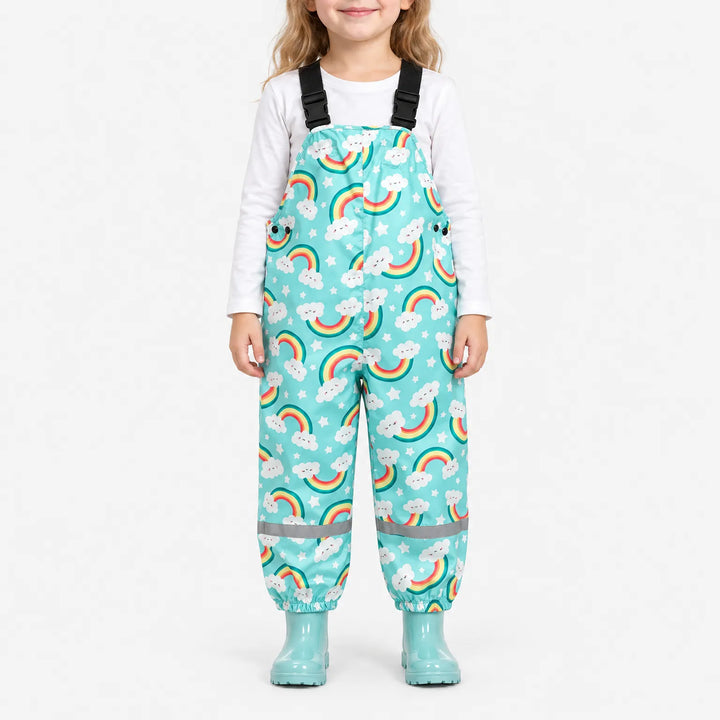 Smiling girl wearing turquoise dungarees printed with smiling clouds, rainbows and stars, with matching turquoise wellies and a white top. 2