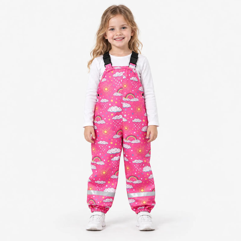 Smiling girl in pink dungarees with a pattern of clouds, rainbows, suns and raindrops, worn with a white top and white trainers. 4