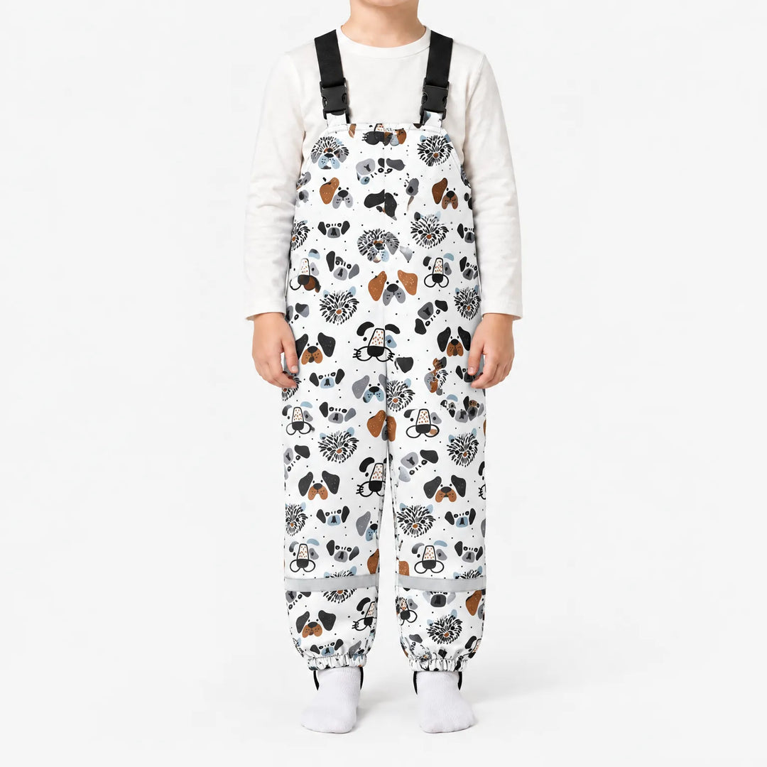 Child standing in white dungarees printed with illustrated dog faces in black, grey and brown, with black buckled straps and reflective ankle bands. 7