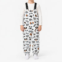 Child standing in white dungarees printed with illustrated dog faces in black, grey and brown, with black buckled straps and reflective ankle bands. 7
