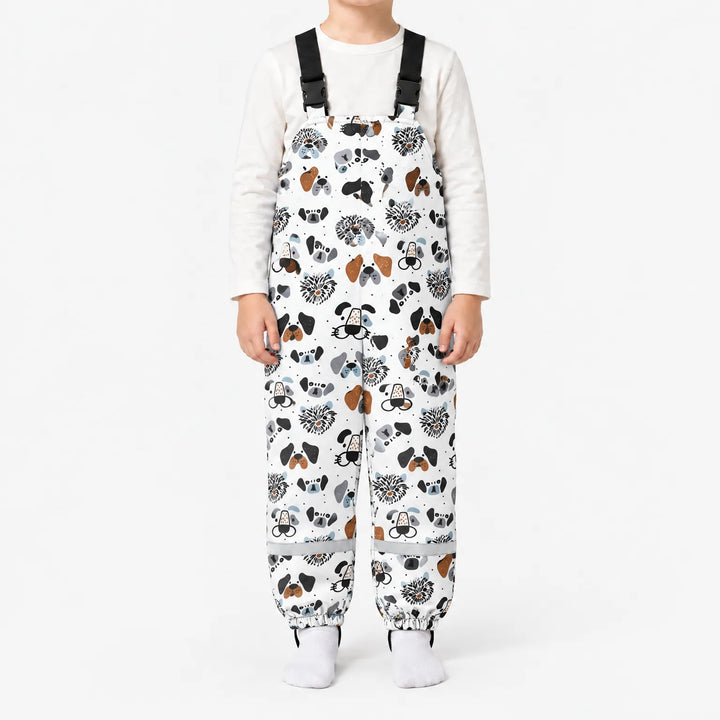 Child standing in white dungarees printed with illustrated dog faces in black, grey and brown, with black buckled straps and reflective ankle bands. 7