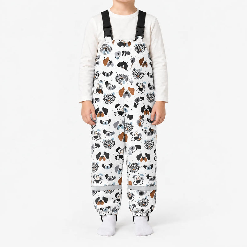 Child standing in white dungarees printed with illustrated dog faces in black, grey and brown, with black buckled straps and reflective ankle bands. 7