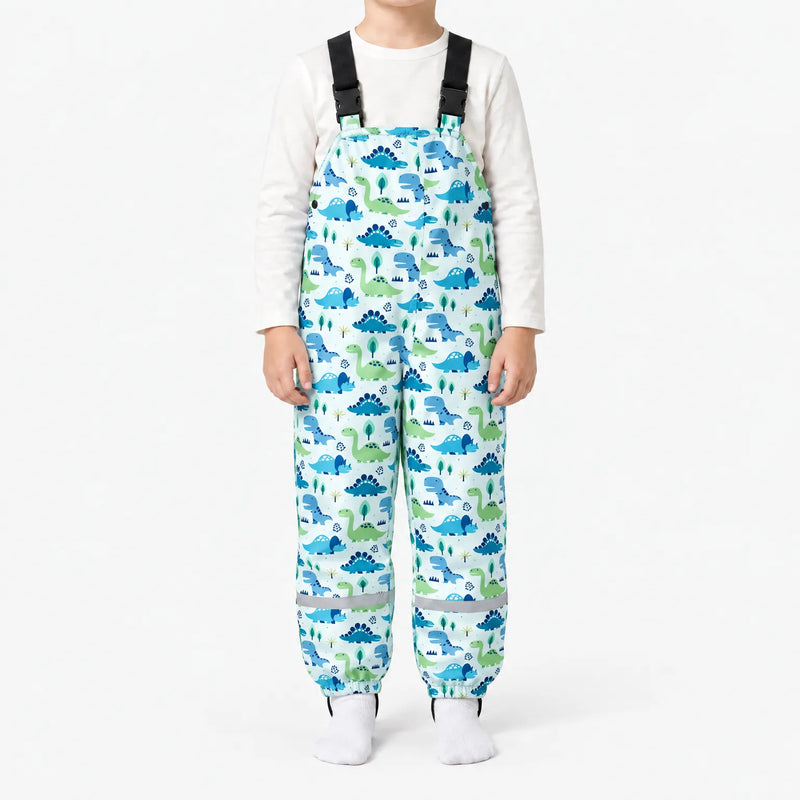 Child in pale blue dungarees printed with blue and green dinosaurs and little trees, with buckled straps and a reflective band at each ankle. 9