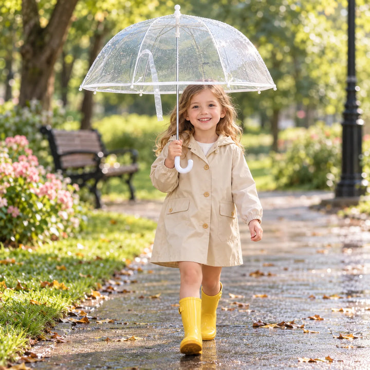 Girl in a beige hooded raincoat and yellow rain boots walks along a wet park path holding the clear umbrella. 3
