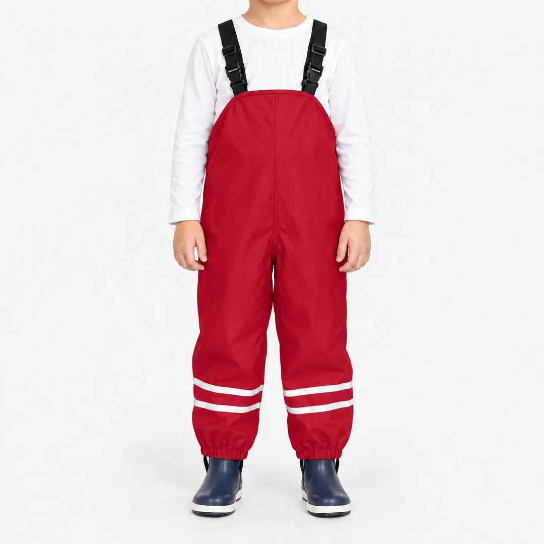 Child facing front in red waterproof dungarees with black buckled straps, reflective leg stripes and navy boots against white. 11