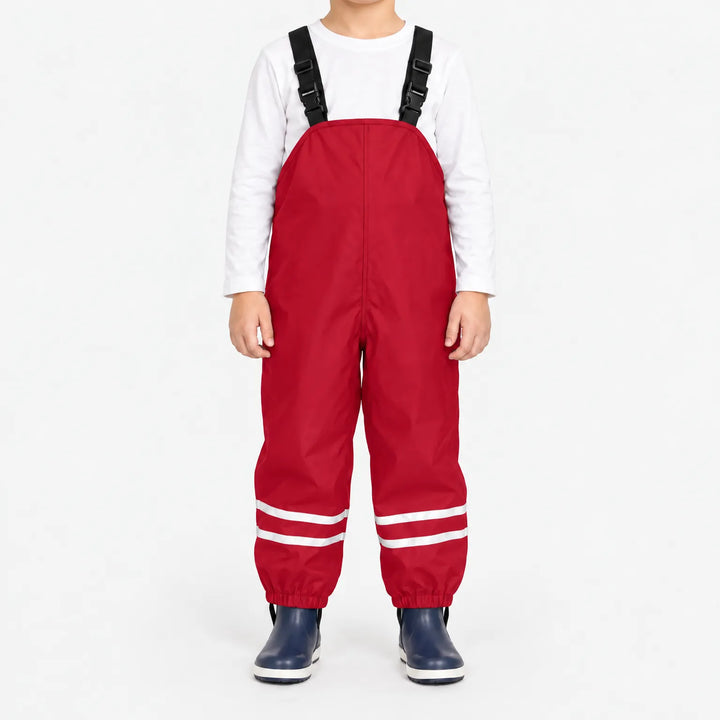 Child facing front in red waterproof dungarees with black buckled straps, reflective leg stripes and navy boots against white. 11