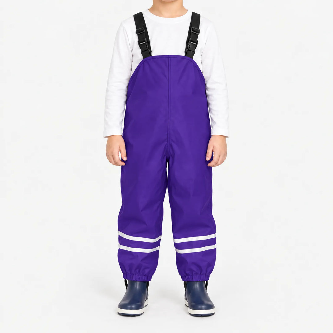 Child facing front in purple waterproof dungarees with adjustable black straps, reflective ankle stripes and navy boots, white background. 12