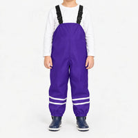 Child facing front in purple waterproof dungarees with adjustable black straps, reflective ankle stripes and navy boots, white background. 12