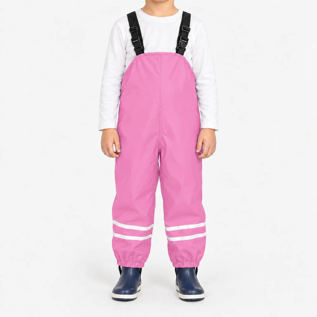 Child facing front in light pink waterproof dungarees with black buckled straps, reflective leg stripes and navy boots, white background. 13