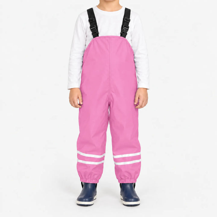 Child facing front in light pink waterproof dungarees with black buckled straps, reflective leg stripes and navy boots, white background. 13