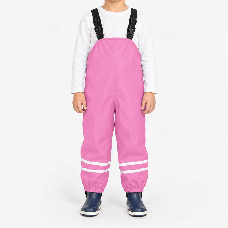 Child facing front in light pink waterproof dungarees with black buckled straps, reflective leg stripes and navy boots, white background. 13