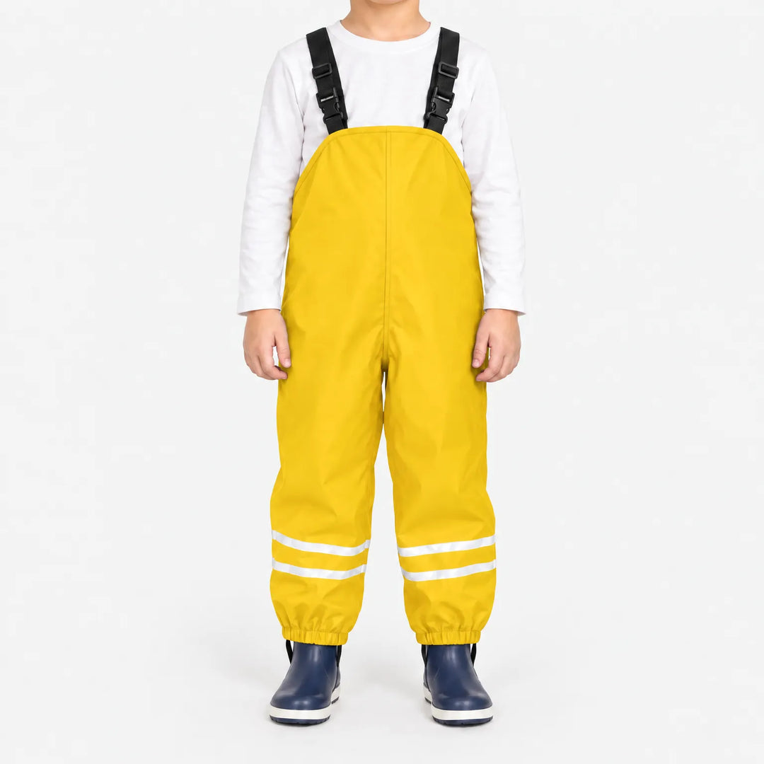 Child facing front in yellow waterproof dungarees with white top, reflective stripes on both legs and navy boots, plain white background. 14