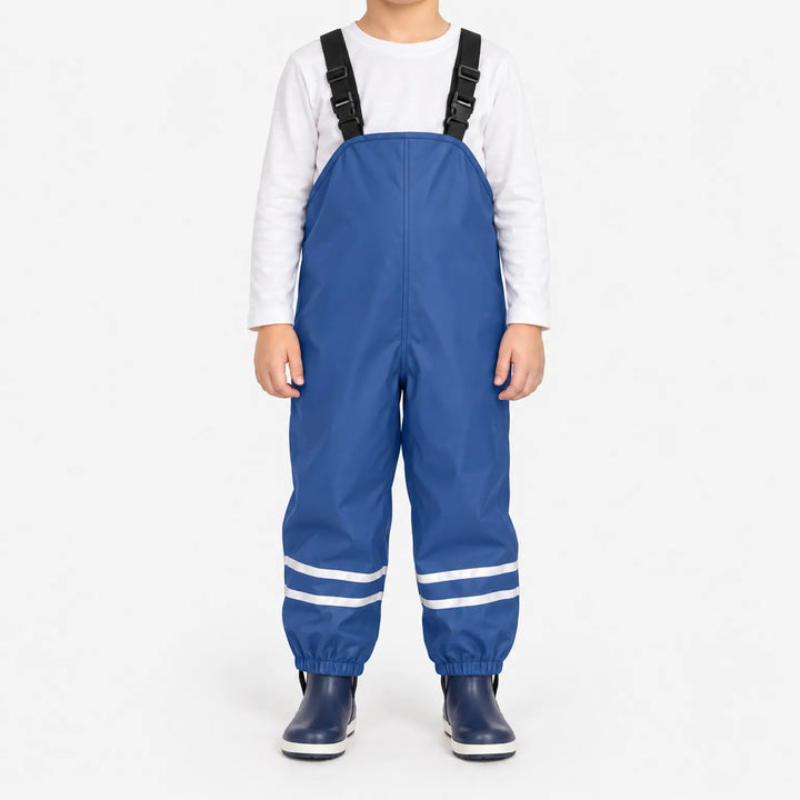 Child facing front in blue waterproof dungarees with adjustable black straps, reflective ankle stripes and navy boots against a white background. 2