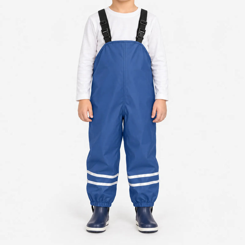 Child facing front in blue waterproof dungarees with adjustable black straps, reflective ankle stripes and navy boots against a white background. 2