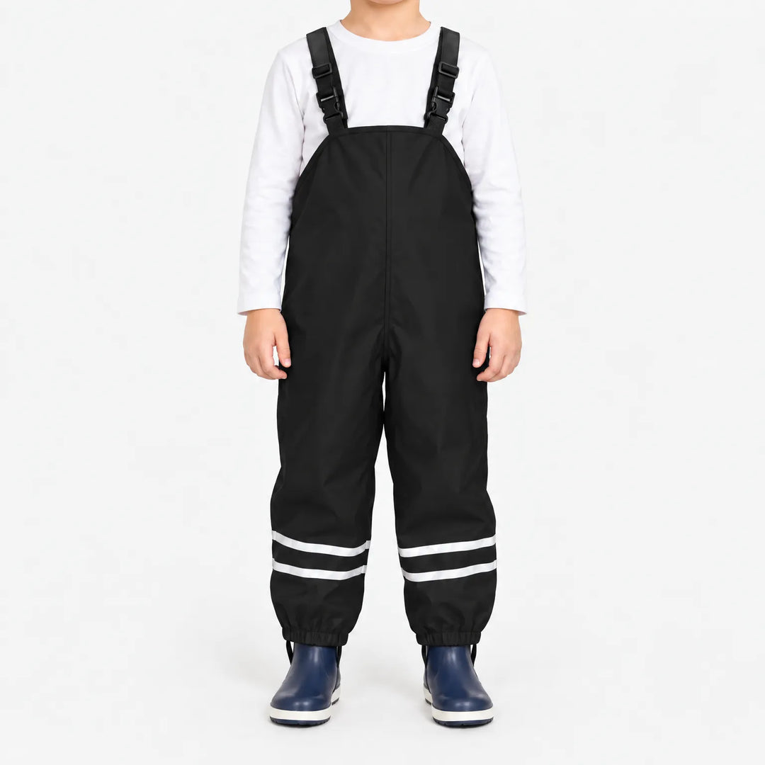 Child facing front in black waterproof dungarees with white long-sleeve top, reflective ankle stripes and navy boots on a white background. 7