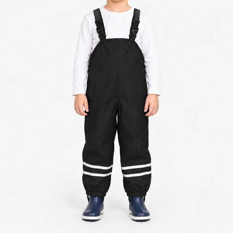 Child facing front in black waterproof dungarees with white long-sleeve top, reflective ankle stripes and navy boots on a white background. 7