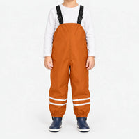 Child facing front in orange waterproof dungarees with black buckled straps, reflective leg stripes and navy boots, white background. 8