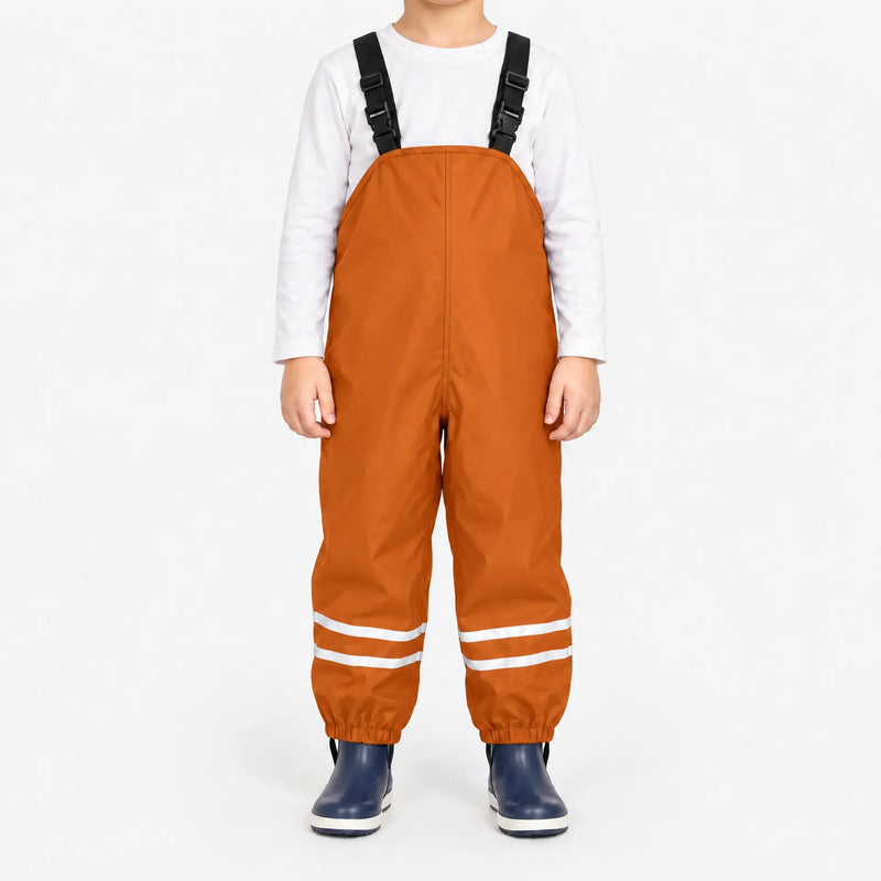 Child facing front in orange waterproof dungarees with black buckled straps, reflective leg stripes and navy boots, white background. 8