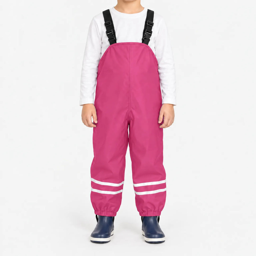 Child facing front in bright pink waterproof dungarees with reflective stripes on each leg and navy boots, plain white background. 9