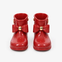 Front view of a pair of glossy red wellies with large bows and gold bands, shown on a plain white background. 2