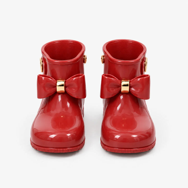 Front view of a pair of glossy red wellies with large bows and gold bands, shown on a plain white background. 2