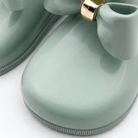 Close-up of the rounded toe and glossy bow with gold band on a sage green welly, showing the ridged sole edge. 6
