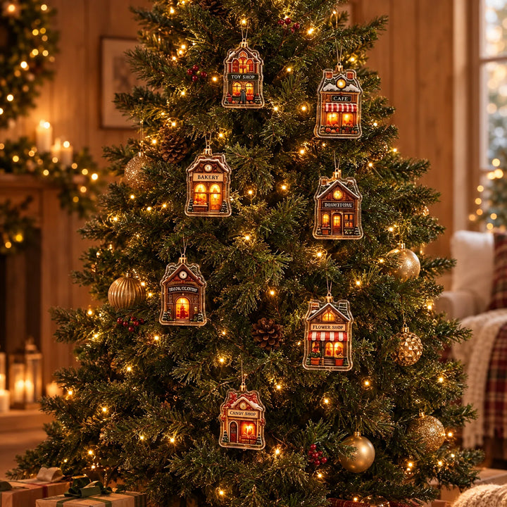 Seven small house-shaped village ornaments with glowing windows hang from a lit Christmas tree decorated with gold baubles, pinecones and red berries. 1