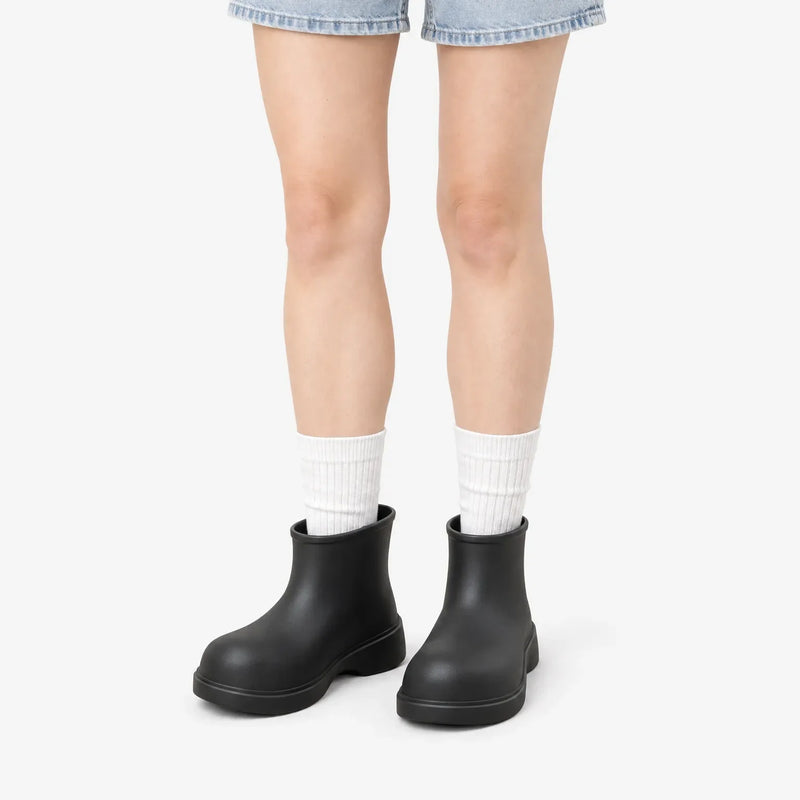 Black ankle boots worn by a model in denim shorts and white ribbed socks against a plain white background. 2