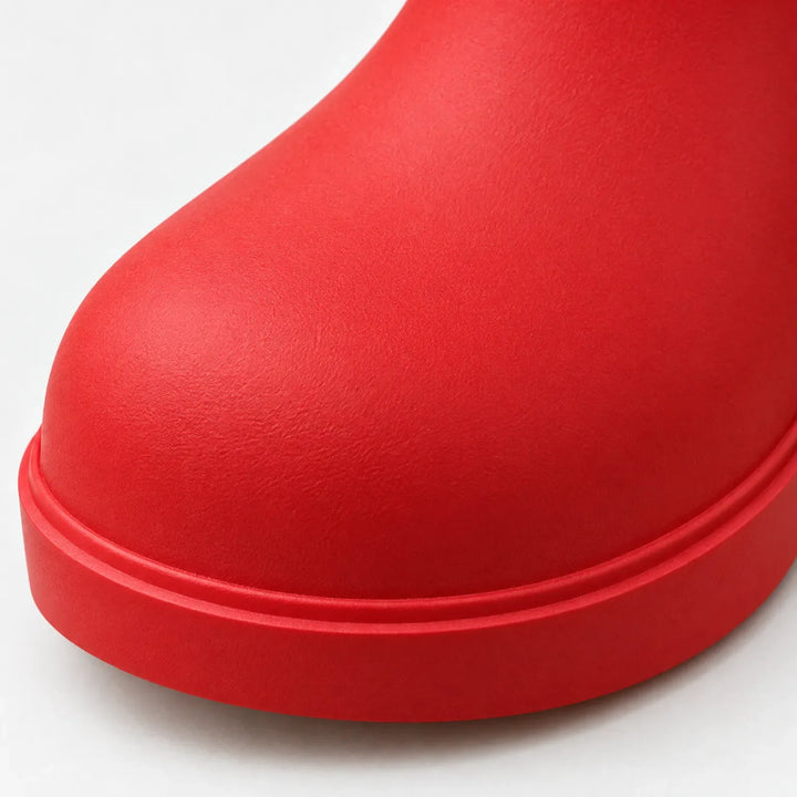 Close-up detail of a red boot toe, showing the smooth matte rubber surface and the raised ridge along the chunky sole. 6