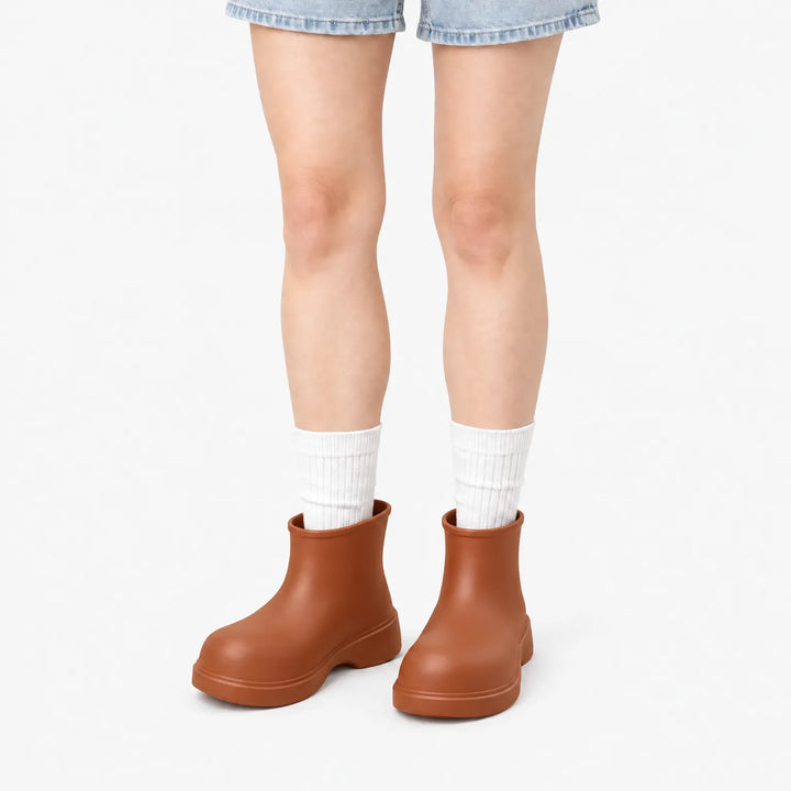 Rust-brown ankle boots worn by a model in denim shorts and white ribbed socks against a plain white background. 7