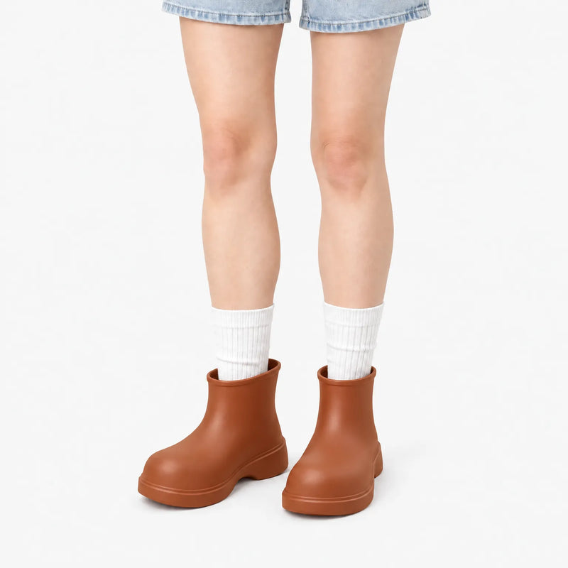Rust-brown ankle boots worn by a model in denim shorts and white ribbed socks against a plain white background. 7