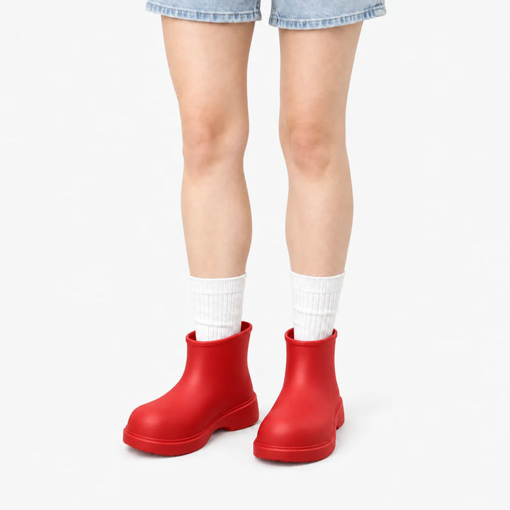 Bright red ankle boots worn by a model in denim shorts and white ribbed socks against a plain white background. 8