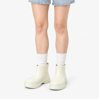 Cream-white ankle boots worn by a model in denim shorts and white ribbed socks against a plain white background. 9