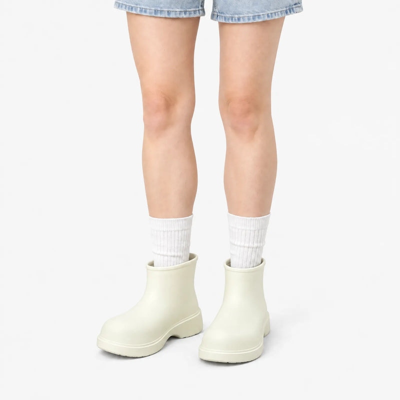 Cream-white ankle boots worn by a model in denim shorts and white ribbed socks against a plain white background. 9