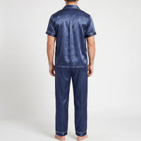 Back view of a model wearing the navy satin pyjama set, showing the shoulder yoke, centre back pleat and piped sleeve and trouser cuffs. 3