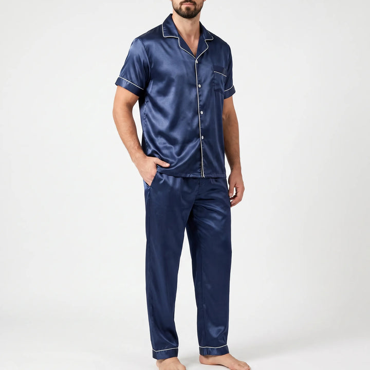 Three-quarter side view of a bearded model in the navy satin pyjama set with white piping, one hand in pocket. 4