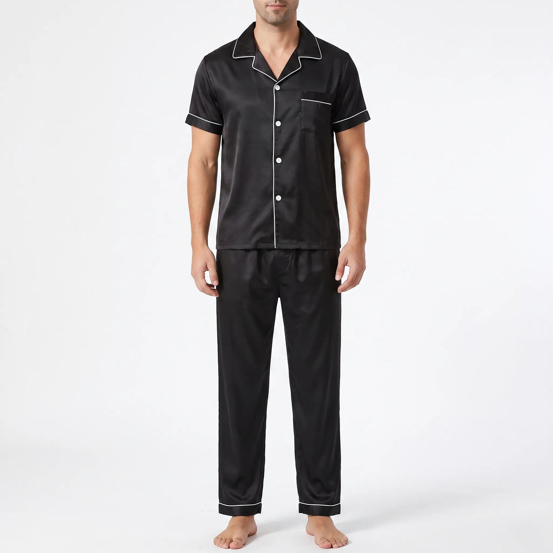 Front view of a model wearing the black satin pyjama set with white piping, button front, chest pocket and long trousers. 6