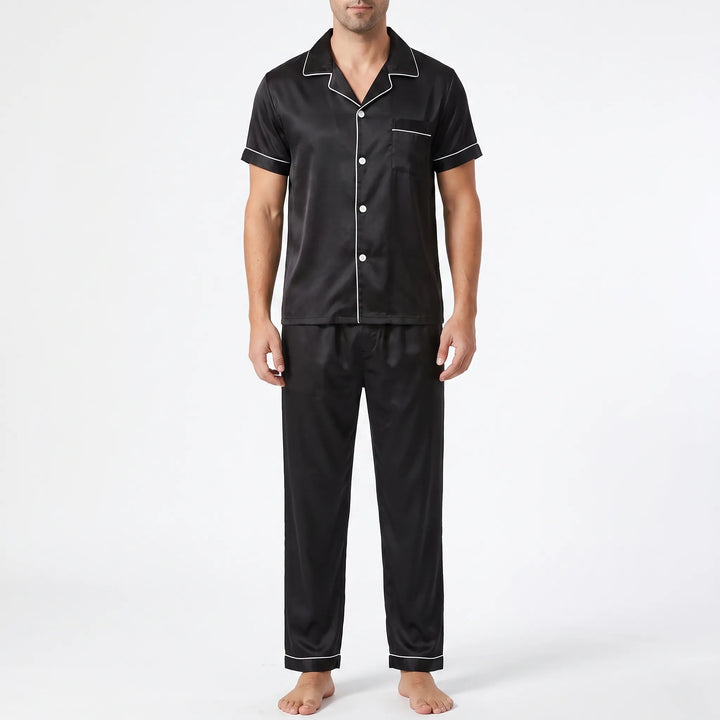 Front view of a model wearing the black satin pyjama set with white piping, button front, chest pocket and long trousers. 6