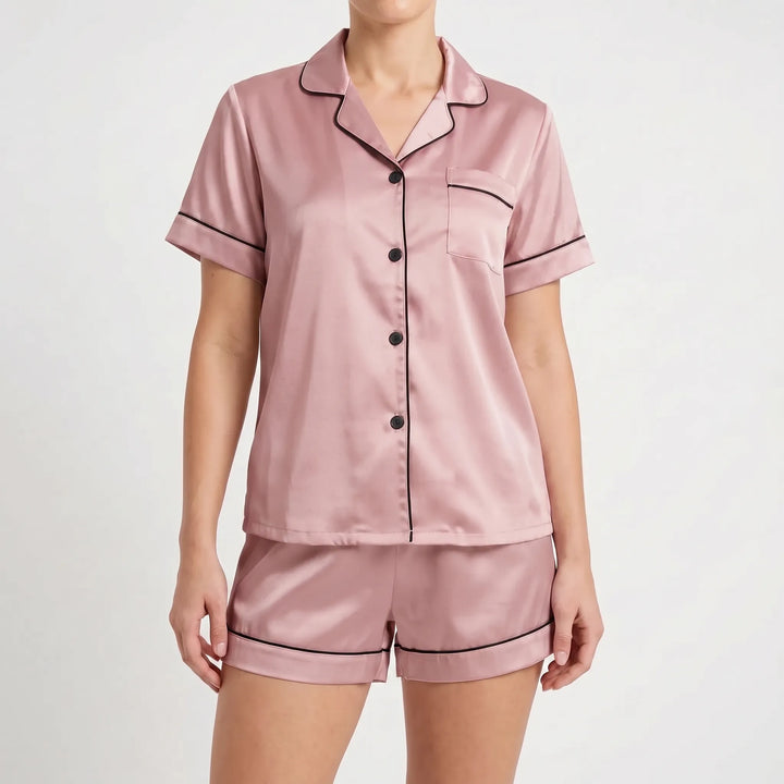 Front view of the dusty pink satin pyjama set with dark piping and black buttons, worn by a model. 8
