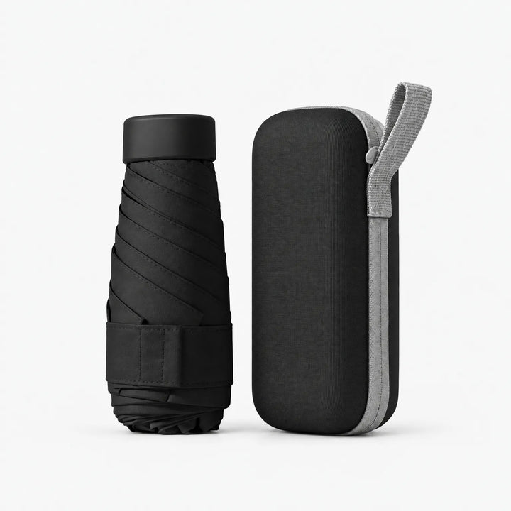 Black folded umbrella with black cap and strap beside a matching black hard zippered case with a light grey wrist loop, on white. 12