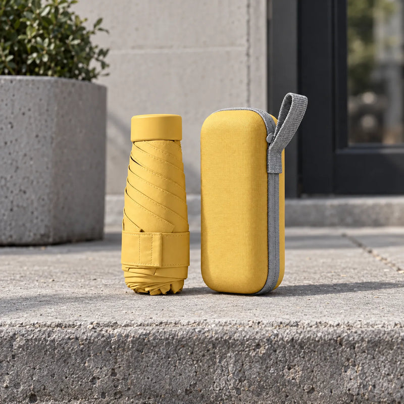 Mustard yellow folded umbrella standing next to its matching hard zip case with grey loop, set on a concrete step outdoors. 3